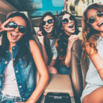 Just fun and road ahead. Four beautiful young cheerful women looking happy and playful while sitting in car