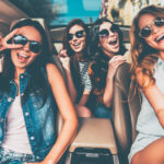 bigstock–125294966 Just fun and road ahead. Four beautiful young cheerful women looking happy and playful while sitting in car