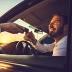 Here are your car keys! Happy businessman taking the car keys from unrecognizable person at sunset.
