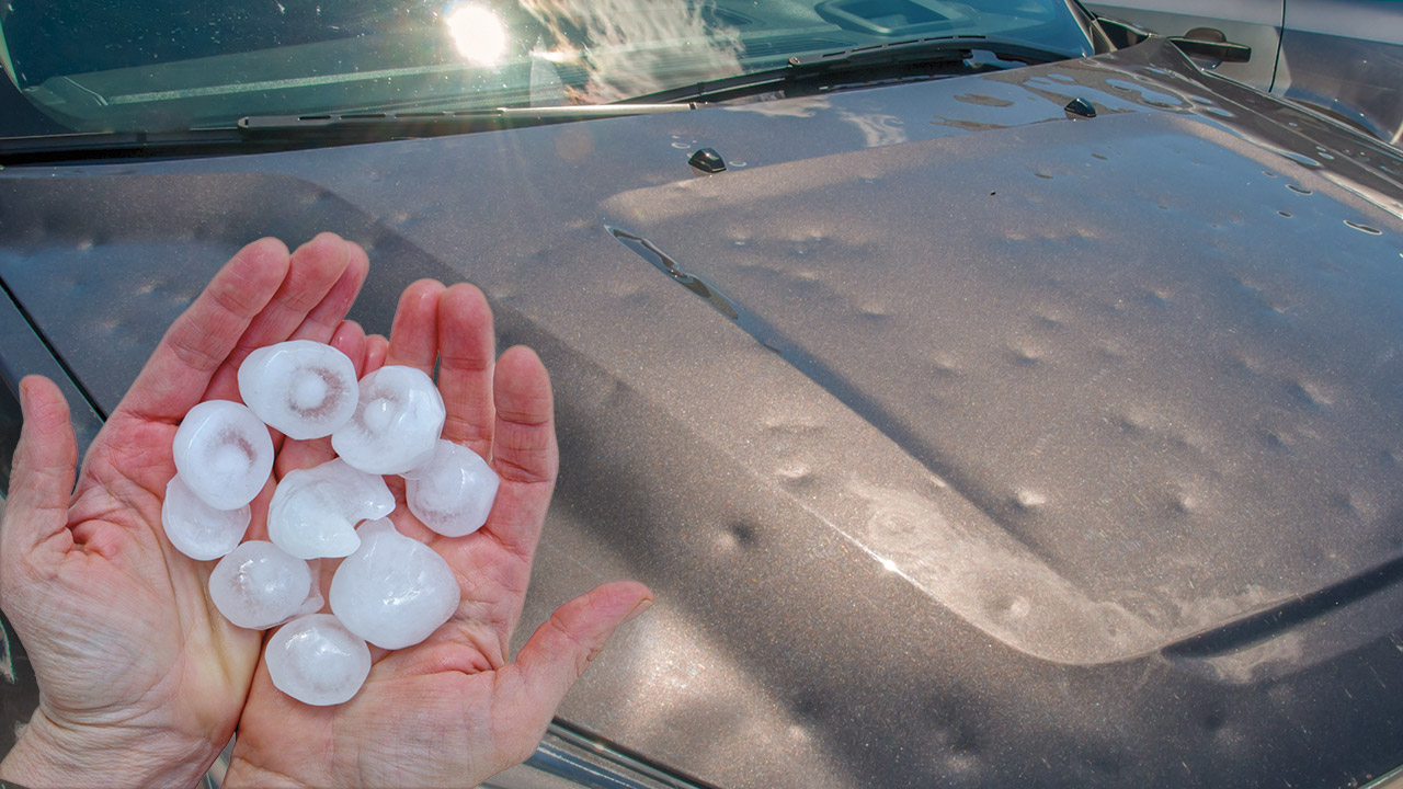 hand holding hail in front of dented car