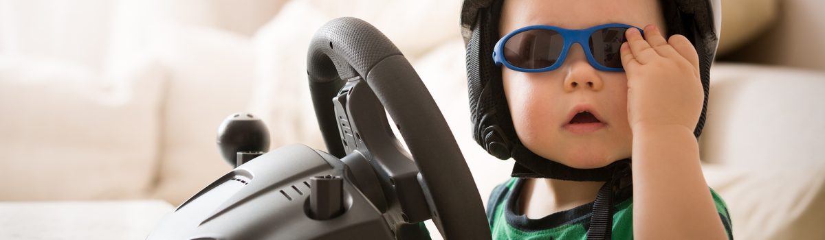 Cute little kid boy in a helmet playing with Computer steering wheel. Future driver. Getting ready for professional driving. Child driving a car. Funny toddler boy indoors. Boy and a car.