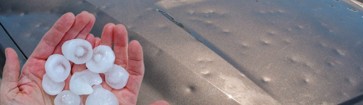 hand holding hail in front of dented car